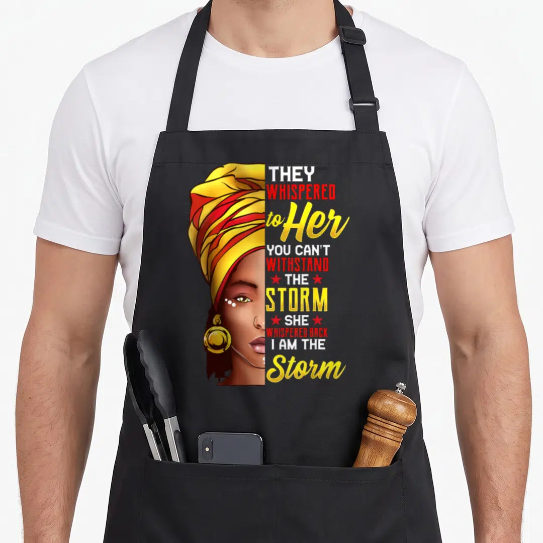 History black apron - Woman in yellow headwrap with text They whispered to her you can't withstand the storm she — shown on a black cotton canvas apron against a white background