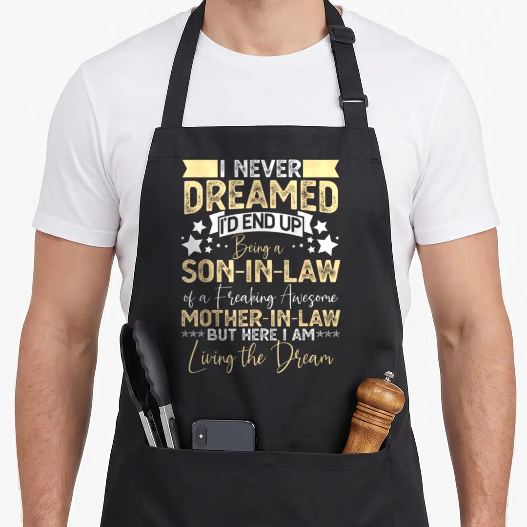 Birthday mother son aprons - Tan and white typography reading I Never Dreamed I'd End Up Being a Son-in-Law — shown on a black cotton canvas apron against a white background