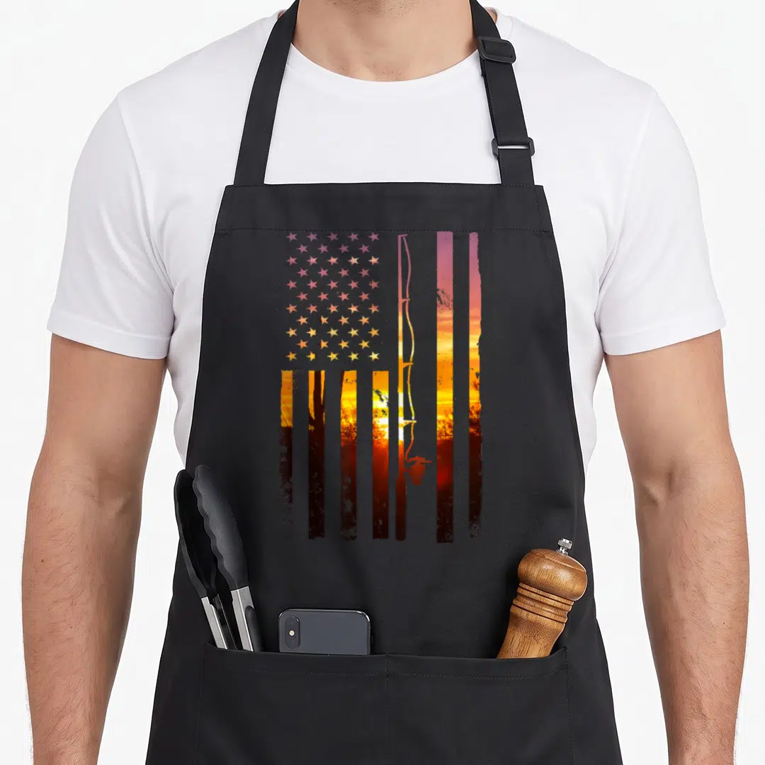 Fisher american flag apron - Distressed USA flag formed by sunset landscape with fishing rod and tree silhouettes — shown on a black cotton canvas apron against a white background
