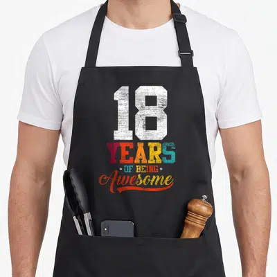 18th bday apron - Stacked 18 YEARS OF BEING Awesome text in white and rainbow gradient colors with vintage texture — shown on a black cotton canvas apron against a white background