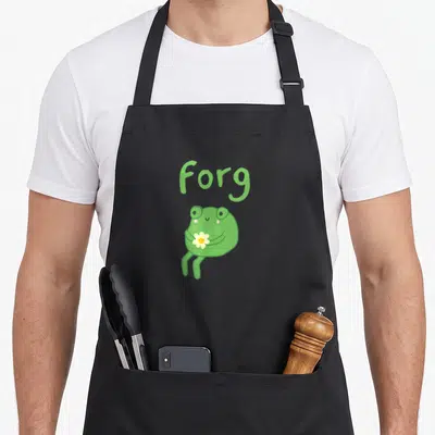 Frog cake apron - Cartoon frog holding white flower below Forg text in green and yellow — shown on a black cotton canvas apron against a white background