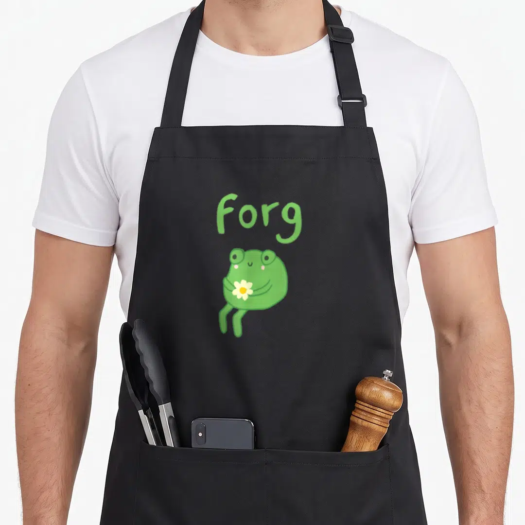 Frog cake apron - Cartoon frog holding white flower below Forg text in green and yellow — shown on a black cotton canvas apron against a white background