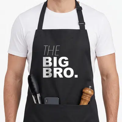 Brother buddy read apron - White stacked text reading THE BIG BRO in bold sans-serif font — shown on a black cotton canvas apron against a white background