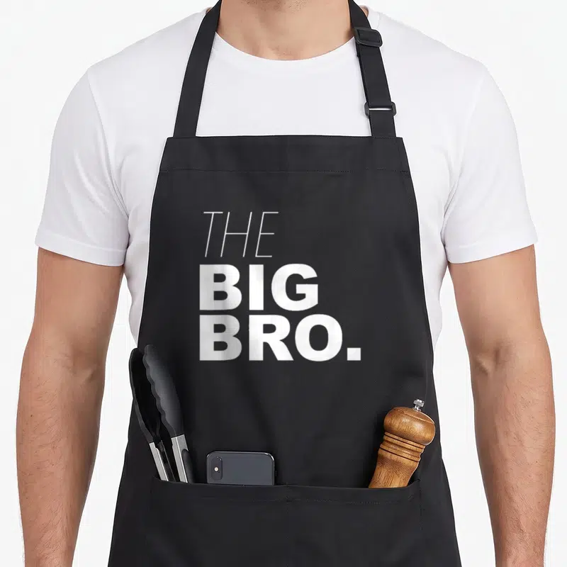 Brother buddy read apron - White stacked text reading THE BIG BRO in bold sans-serif font — shown on a black cotton canvas apron against a white background