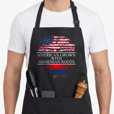Armenian american flag apron - Tree with US flag canopy and Armenian roots separated by text AMERICAN GROWN — shown on a black cotton canvas apron against a white background
