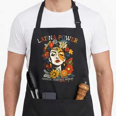 Heritage hispanic aprons - Woman face surrounded by orange yellow blue cream flowers with LATINA POWER and HISPANIC — shown on a black cotton canvas apron against a white background