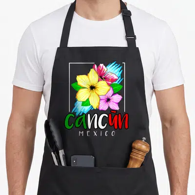 Cancun spring aprons - Cartoon flowers in yellow pink red with cancun MEXICO text and white frame — shown on a black cotton canvas apron against a white background