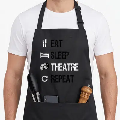 Eat theater apron - Stacked text EAT SLEEP THEATRE REPEAT with fork bed mask and recycle icons in black and white — shown on a black cotton canvas apron against a white background