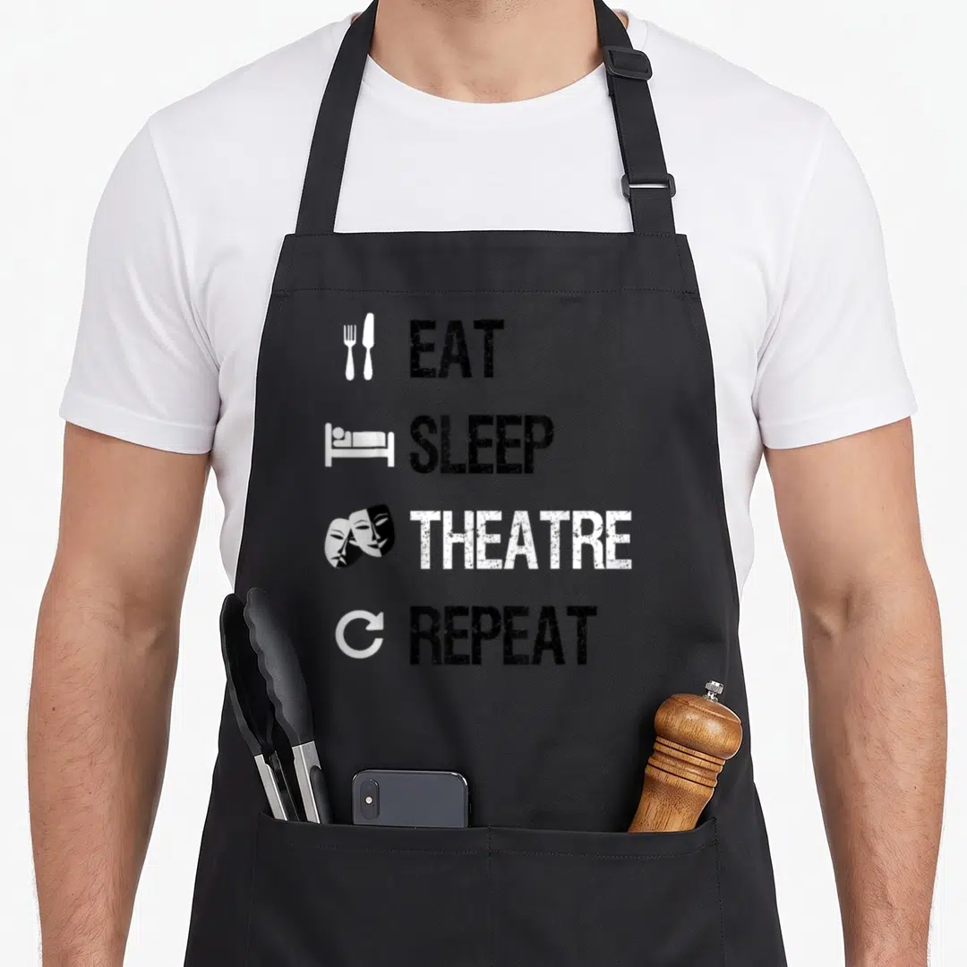 Eat theater apron - Stacked text EAT SLEEP THEATRE REPEAT with fork bed mask and recycle icons in black and white — shown on a black cotton canvas apron against a white background
