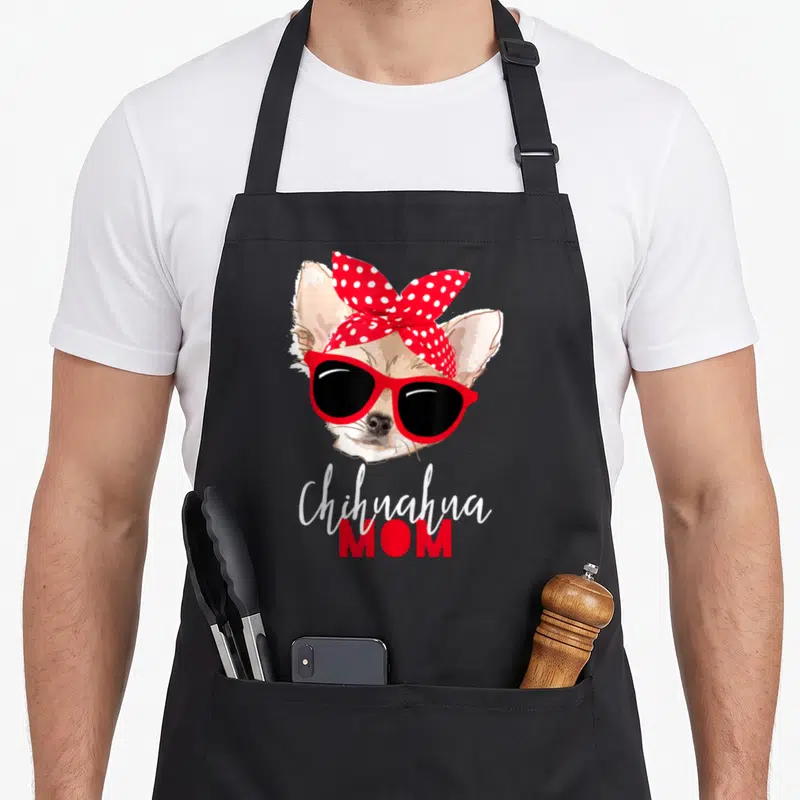 Chihuahua dog mom apron - Cartoon chihuahua face with red sunglasses and polka dot bow above text — shown on a black cotton canvas apron against a white background