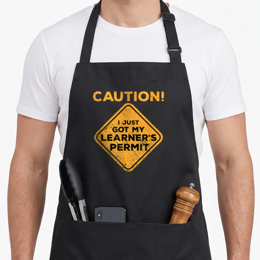 Permit driving apron - Yellow diamond caution sign with black text reading I just got my learner's permit — shown on a black cotton canvas apron against a white background