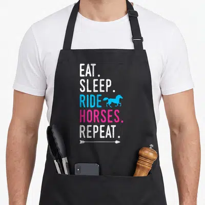 Eat horse apron - Vertical EAT SLEEP RIDE HORSES REPEAT text with blue horse and white arrow — shown on a black cotton canvas apron against a white background