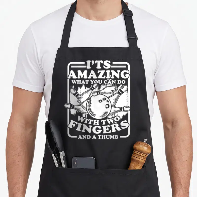 Alley pins for aprons - White distressed bowling ball graphic with text about two fingers and a thumb inside a rounded — shown on a black cotton canvas apron against a white background