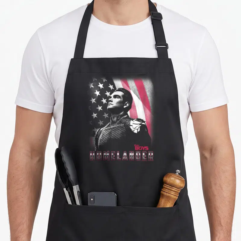 Homelander patriotic aprons - Distressed Homelander portrait over red white grey flag with stacked text — shown on a black cotton canvas apron against a white background