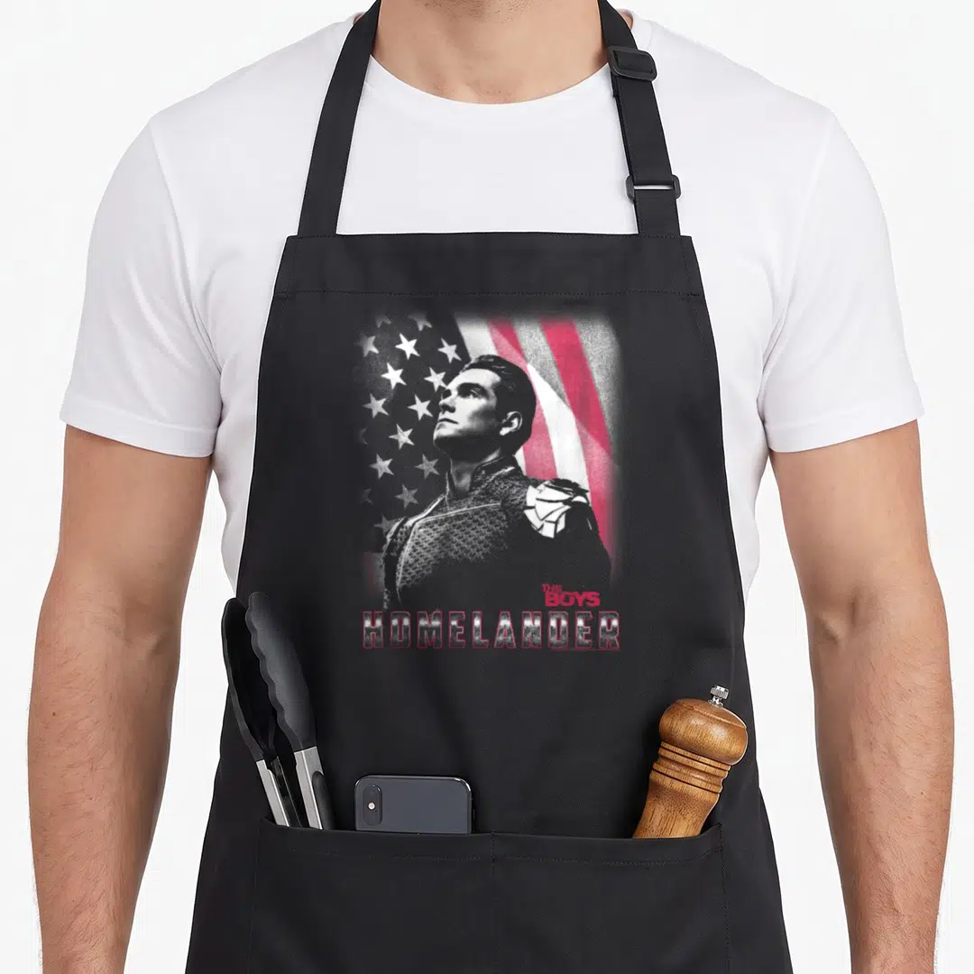 Homelander patriotic aprons - Distressed Homelander portrait over red white grey flag with stacked text — shown on a black cotton canvas apron against a white background