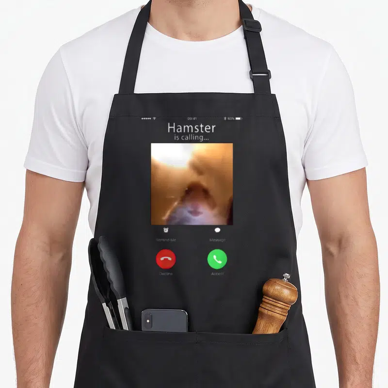Dank meme apron - Smartphone call screen with blurry brown hamster photo, grey background, red and green buttons — shown on a black cotton canvas apron against a white background