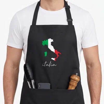 Italia travel aprons - Minimalist map of Italy filled with green white and red flag colors above white script text — shown on a black cotton canvas apron against a white background