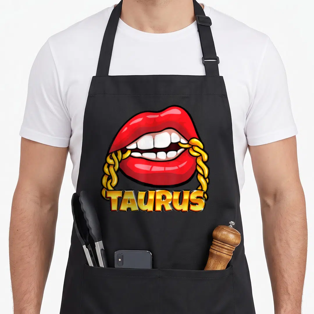 Juicy taurus aprons - Red cartoon lips biting a gold chain with TAURUS text below — shown on a black cotton canvas apron against a white background
