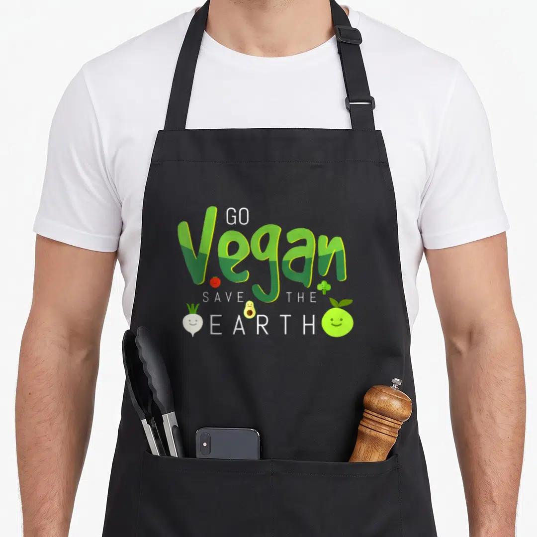 Earth vegan apron - GO Vegan SAVE THE EARTH text with cartoon tomato, broccoli, avocado, turnip, and lime — shown on a black cotton canvas apron against a white background