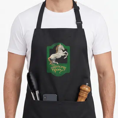 Prancing pull girl apron - Rearing horse in green frame with distressed orange text reading The Prancing Pony — shown on a black cotton canvas apron against a white background