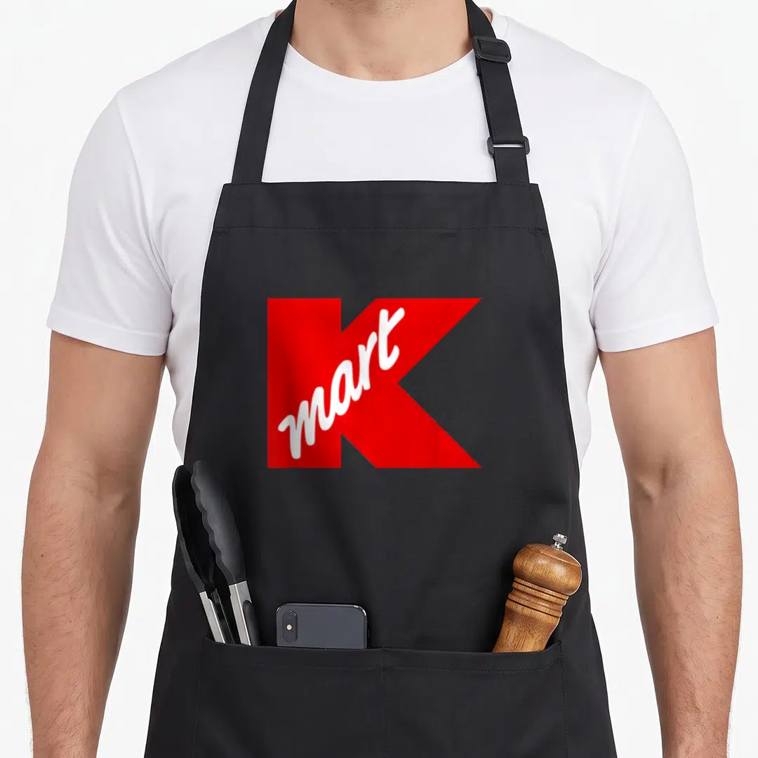 Department kmart apron - Large red letter K background with white mart script written diagonally across the front — shown on a black cotton canvas apron against a white background