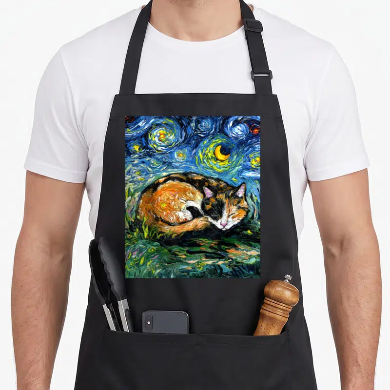Sleeping cat apron - Realistic calico cat sleeping on green grass under swirling blue night sky with moon and stars — shown on a black cotton canvas apron against a white background