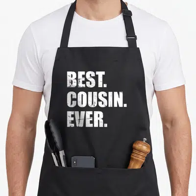 Vintage cousin apron - White distressed text reading BEST. COUSIN. EVER. stacked in three lines — shown on a black cotton canvas apron against a white background