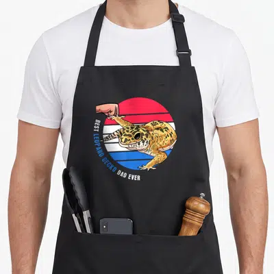 Pet gecko leopard apron - Cartoon gecko over red white blue stripes with text BEST LEOPARD GECKO DAD EVER — shown on a black cotton canvas apron against a white background