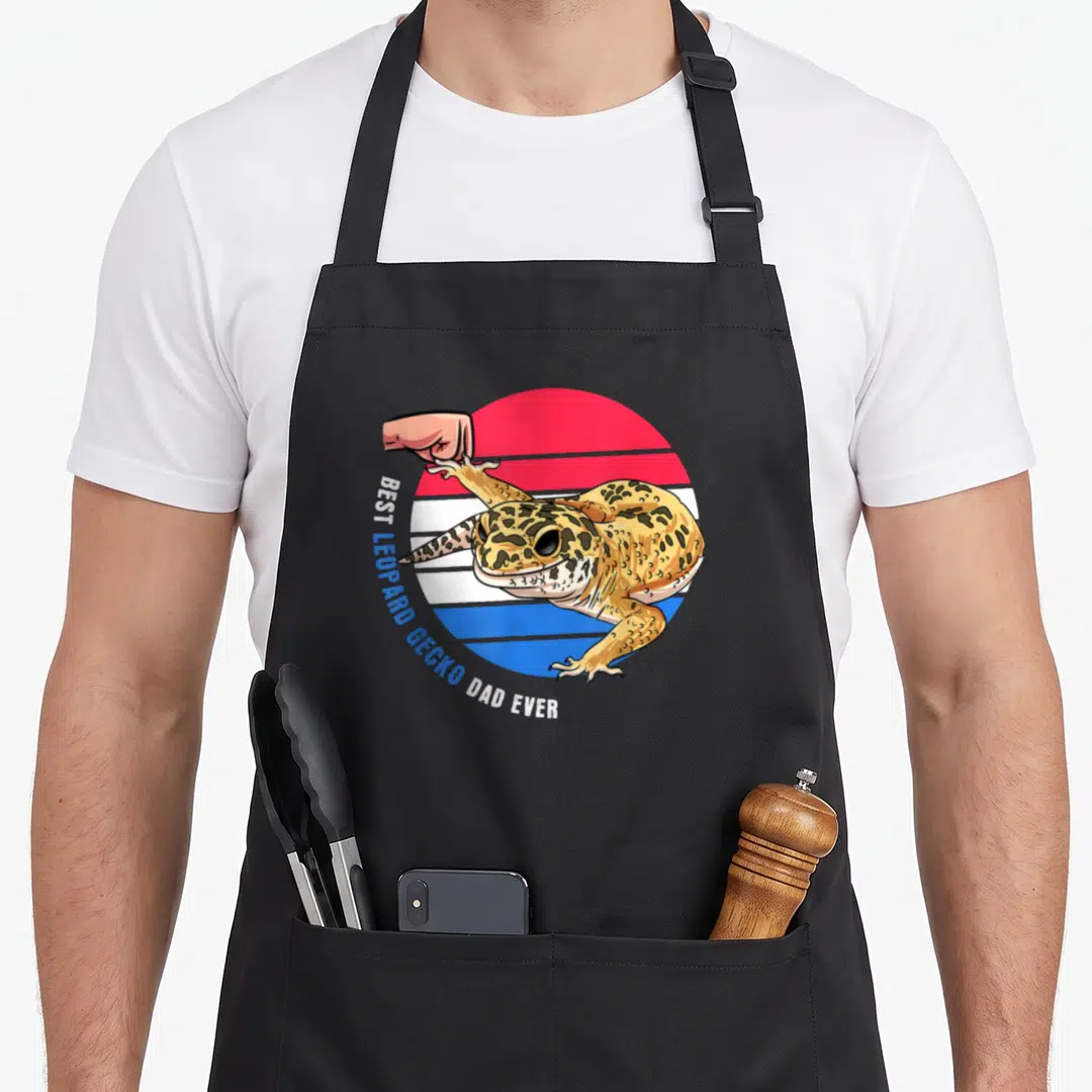 Pet gecko leopard apron - Cartoon gecko over red white blue stripes with text BEST LEOPARD GECKO DAD EVER — shown on a black cotton canvas apron against a white background