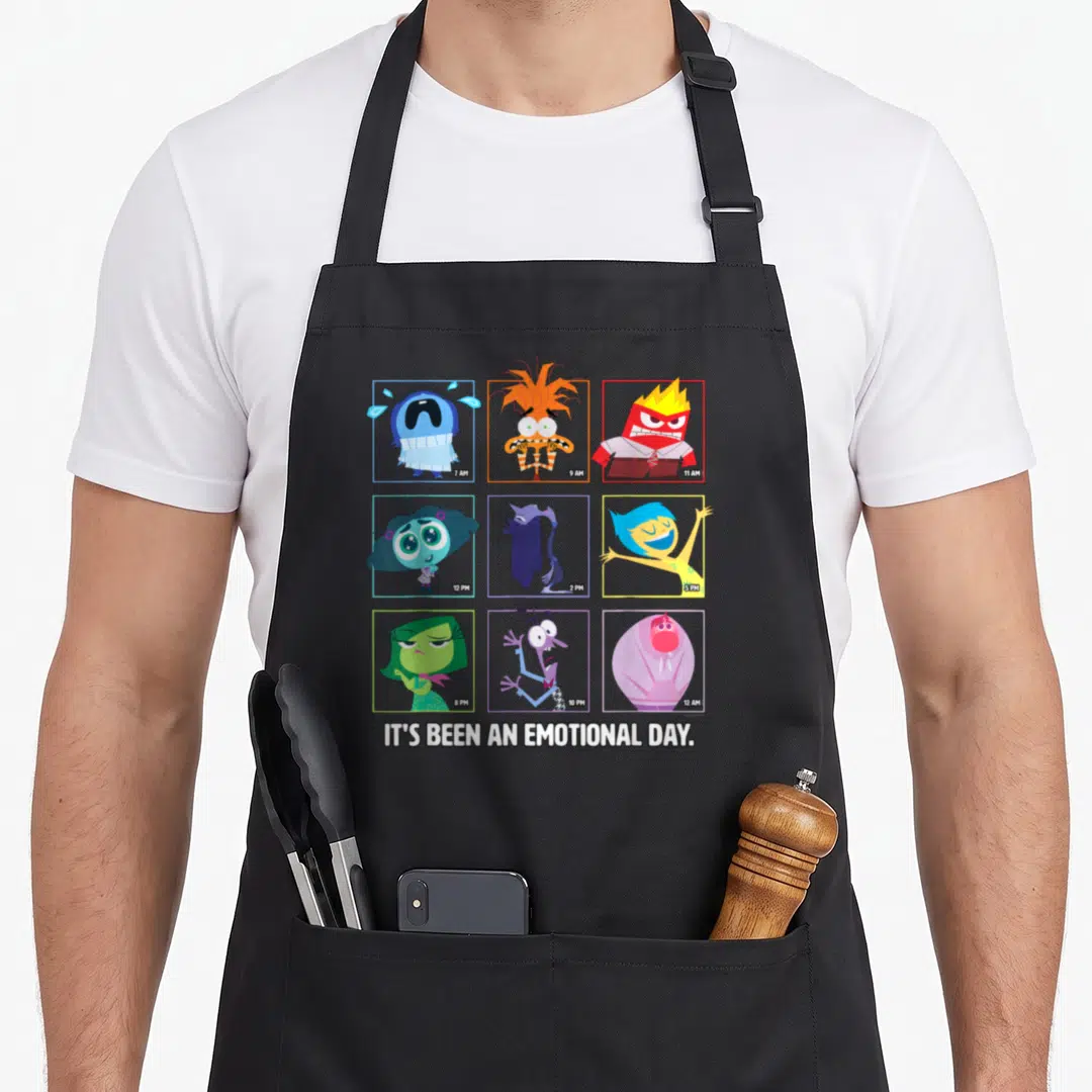 Emotion novelty apron - Nine cartoon characters in colored squares with time stamps above text IT'S BEEN AN EMOTIONAL — shown on a black cotton canvas apron against a white background