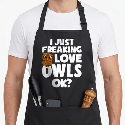 Freaking owl apron - Brown cartoon owl next to stacked white text reading I Just Freaking Love Owls Ok — shown on a black cotton canvas apron against a white background