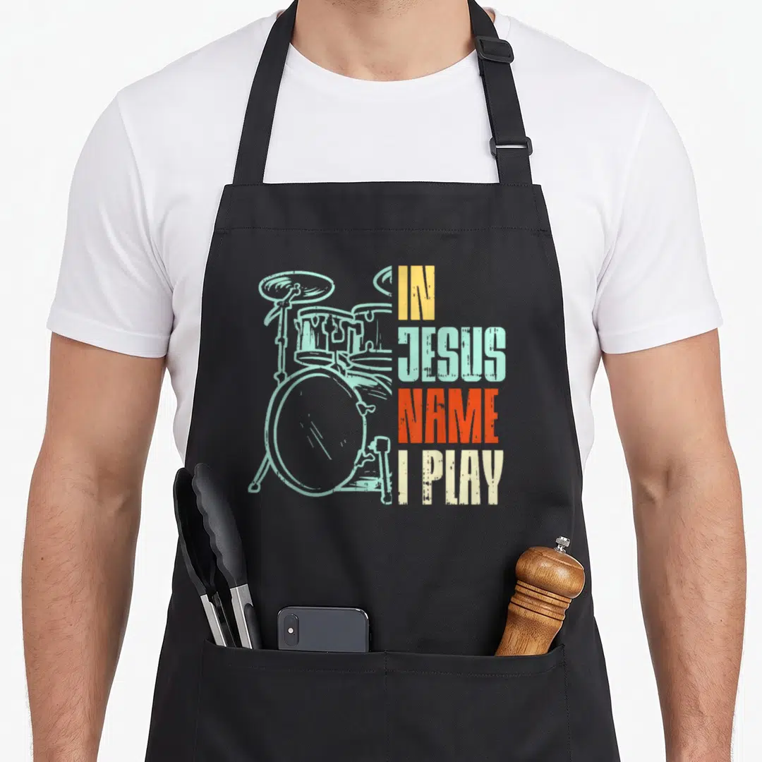 Play christian apron - drum kit in light blue next to four stacked colored words IN JESUS NAME I PLAY — shown on a black cotton canvas apron against a white background