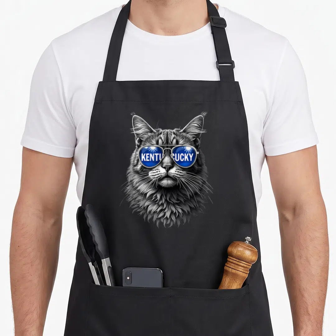 Kentucky cat apron - Realistic grey cat face wearing blue sunglasses with KENTUCKY text across the lenses — shown on a black cotton canvas apron against a white background
