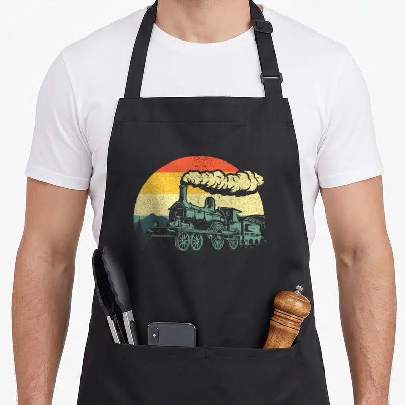 Railroad vintage steam apron - Retro teal steam locomotive with orange and yellow sun and mountains — shown on a black cotton canvas apron against a white background