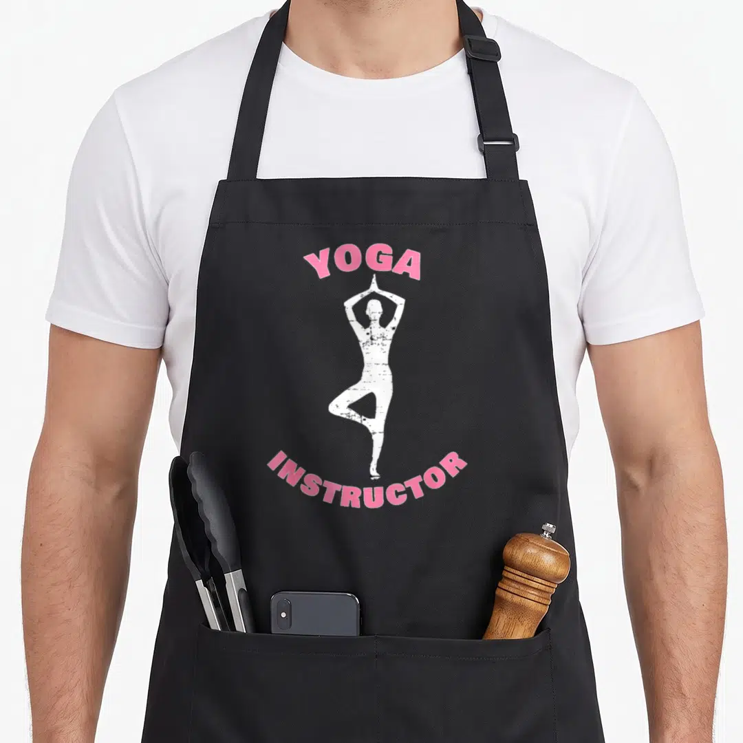 Funny yoga grill instructor apron - White tree pose silhouette between arched pink YOGA INSTRUCTOR text — shown on a black cotton canvas apron against a white background