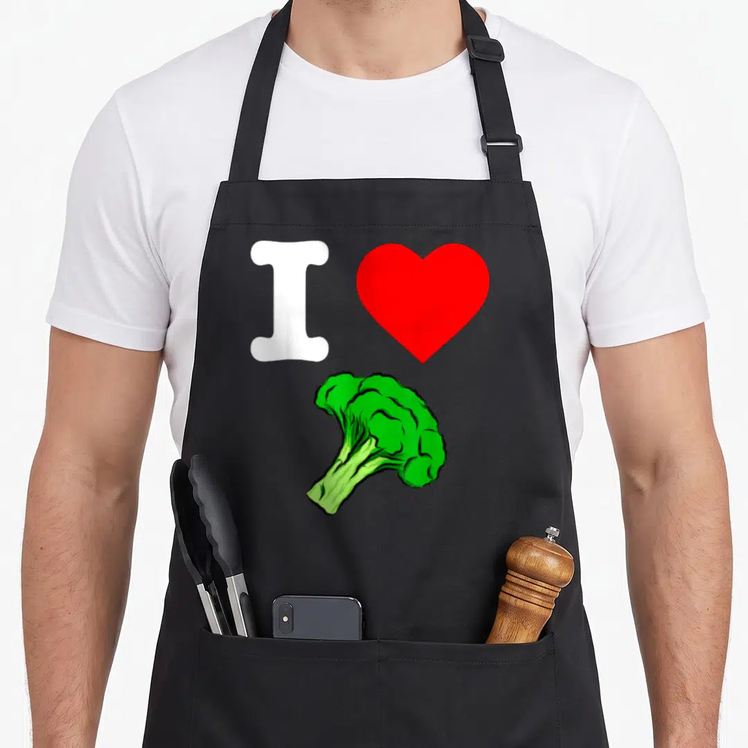 Organic vegetable apron - White I, red heart, and green cartoon broccoli floret on black fabric — shown on a black cotton canvas apron against a white background