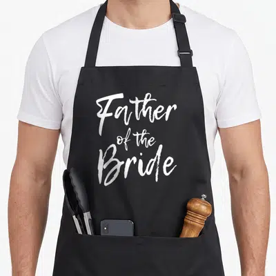 Family father bridal apron - White Father of the Bride script text stacked vertically — shown on a black cotton canvas apron against a white background