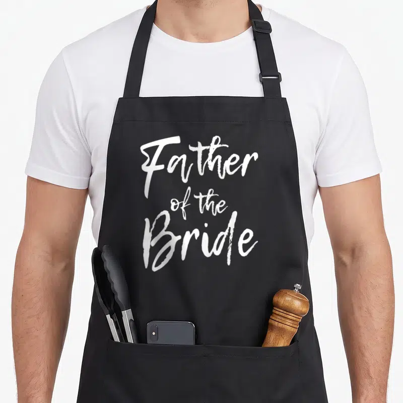 Family father bridal apron - White Father of the Bride script text stacked vertically — shown on a black cotton canvas apron against a white background
