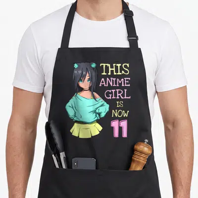 Kawaii anime mom apron - Anime girl with cat ears beside stacked text reading THIS ANIME GIRL IS NOW 11 — shown on a black cotton canvas apron against a white background
