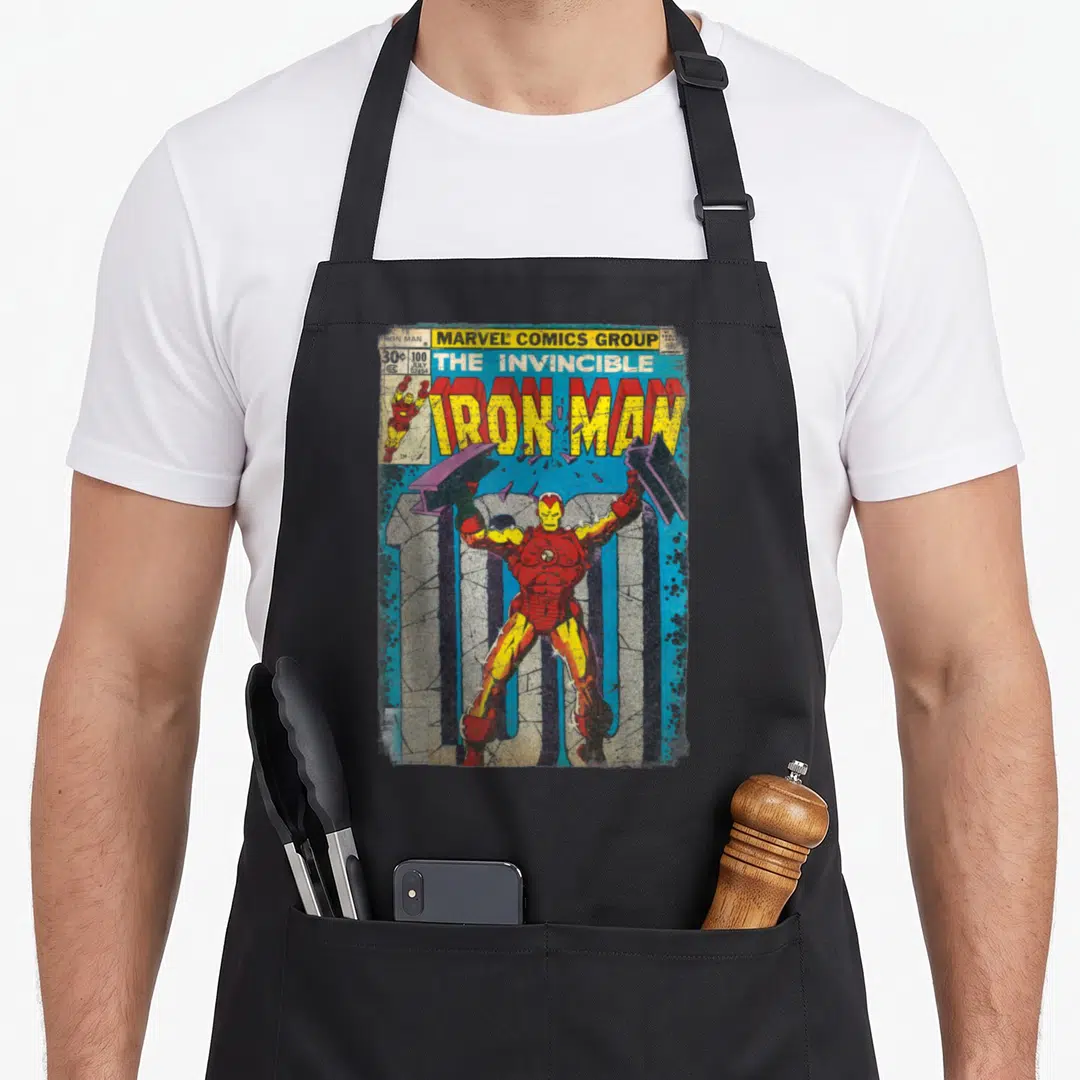 Funny comic cover apron - Iron Man holding two hammers over number 100 in red yellow and blue retro art style — shown on a black cotton canvas apron against a white background