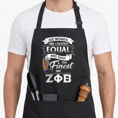 Phi sisterhood apron - Text reading ALL WOMEN ARE CREATED EQUAL BUT ONLY THE Finest ARE ZΦB with ribbon and hand — shown on a black cotton canvas apron against a white background