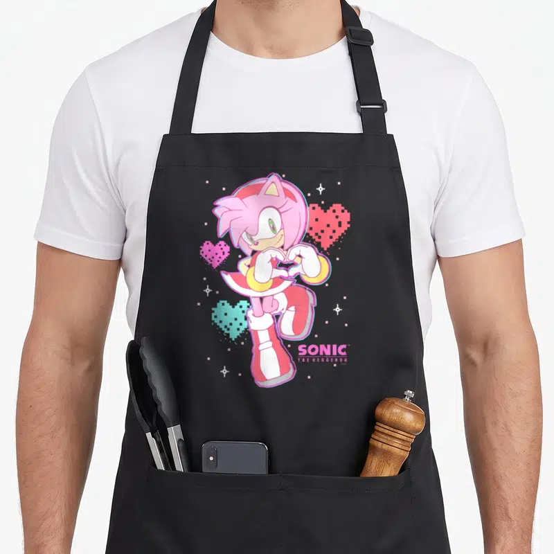 Valentine rose apron - Amy Rose pixel art making heart shape with pink and cyan hearts and Sonic logo — shown on a black cotton canvas apron against a white background