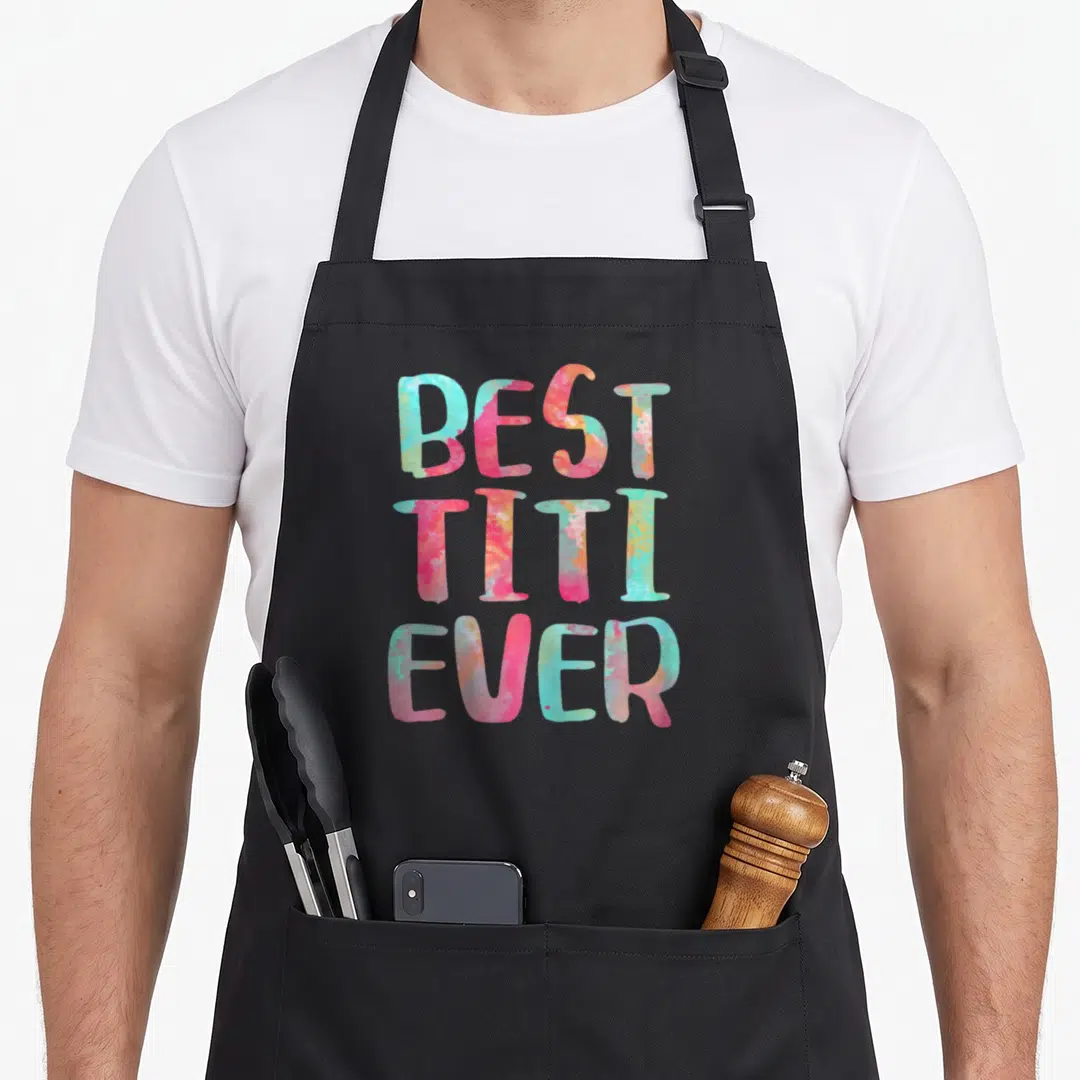 Titi mother's day aprons - Stacked text reading Best Titi Ever in pink teal and orange watercolor font — shown on a black cotton canvas apron against a white background