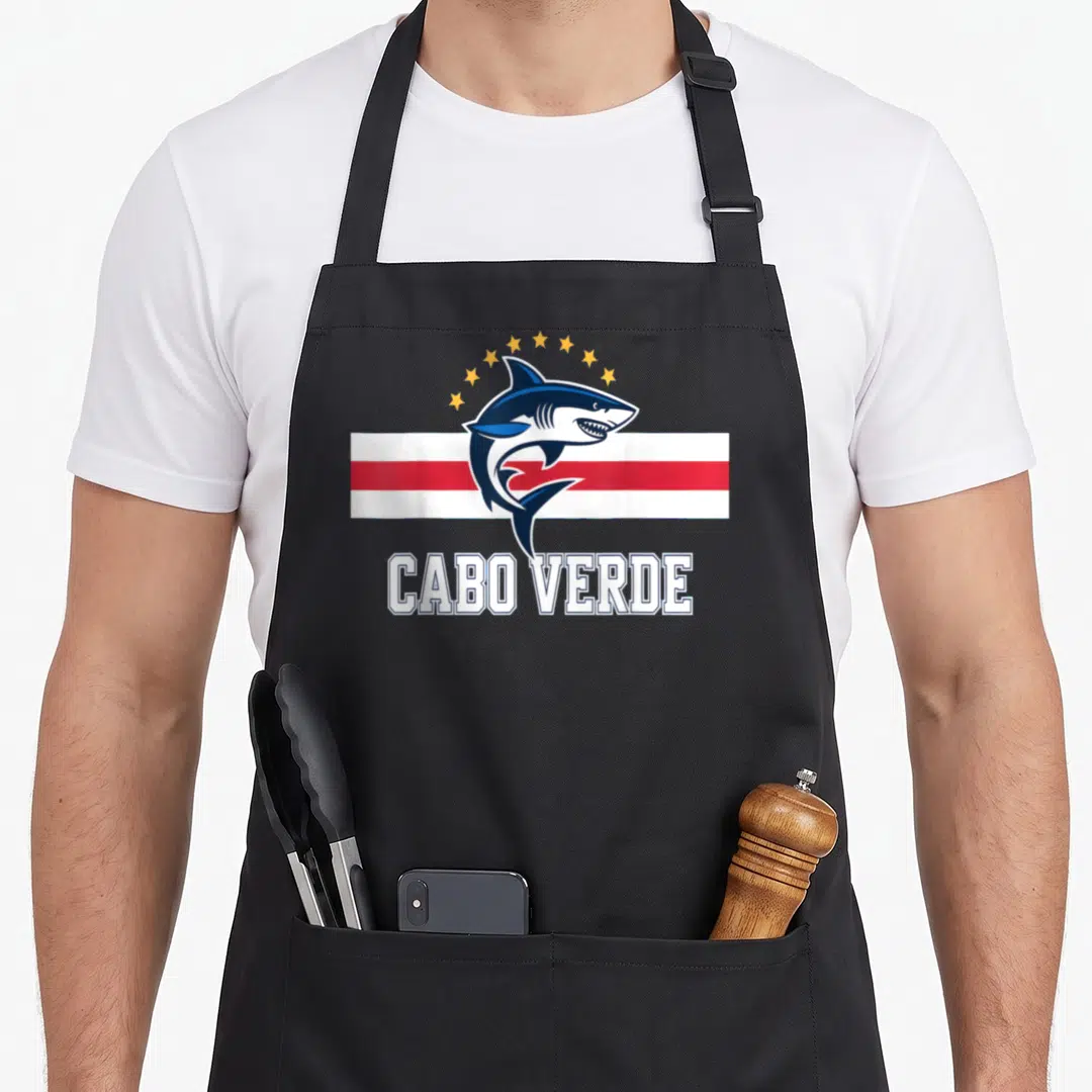 Cabo country apron - Cartoon shark leaping over striped flag with arch of stars and CABO VERDE text below — shown on a black cotton canvas apron against a white background
