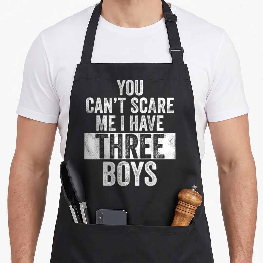 Cute scare dad and son aprons - White stacked text You Can't Scare Me I Have Three Boys distressed style — shown on a black cotton canvas apron against a white background