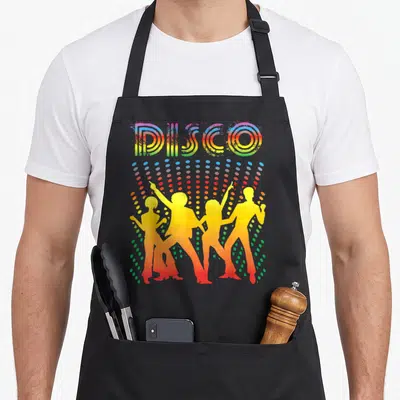 Dancing disco apron - Retro DISCO lettering above four yellow dancer silhouettes and multicolored dot pattern — shown on a black cotton canvas apron against a white background