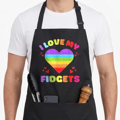Push fidget apron - Rainbow pop-it heart with I LOVE MY FIDGETS text and small red hearts scattered around — shown on a black cotton canvas apron against a white background