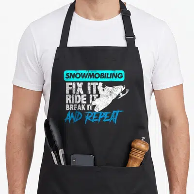 Gear snowmobile girl apron - Cyan box SNOWMOBILING text above white snowmobile silhouette and stacked fix ride break — shown on a black cotton canvas apron against a white background