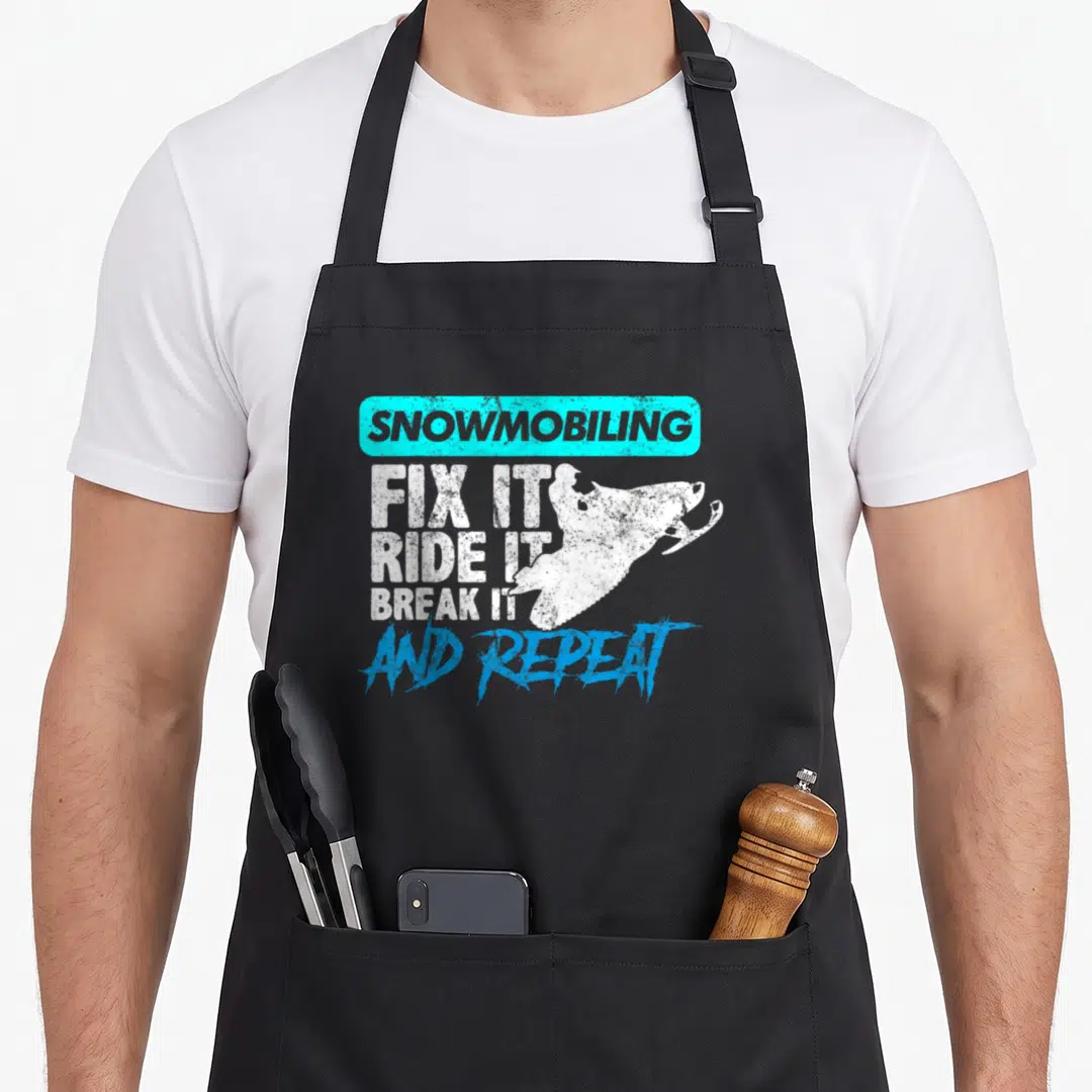 Gear snowmobile girl apron - Cyan box SNOWMOBILING text above white snowmobile silhouette and stacked fix ride break — shown on a black cotton canvas apron against a white background