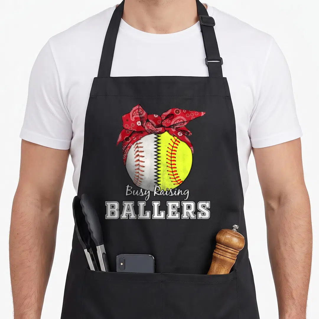 Raising busy apron - Split yellow and white ball with red bandana and Busy Raising Ballers text — shown on a black cotton canvas apron against a white background